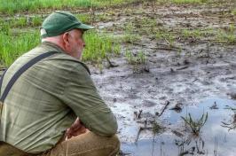 Male farmer squats before flooded field